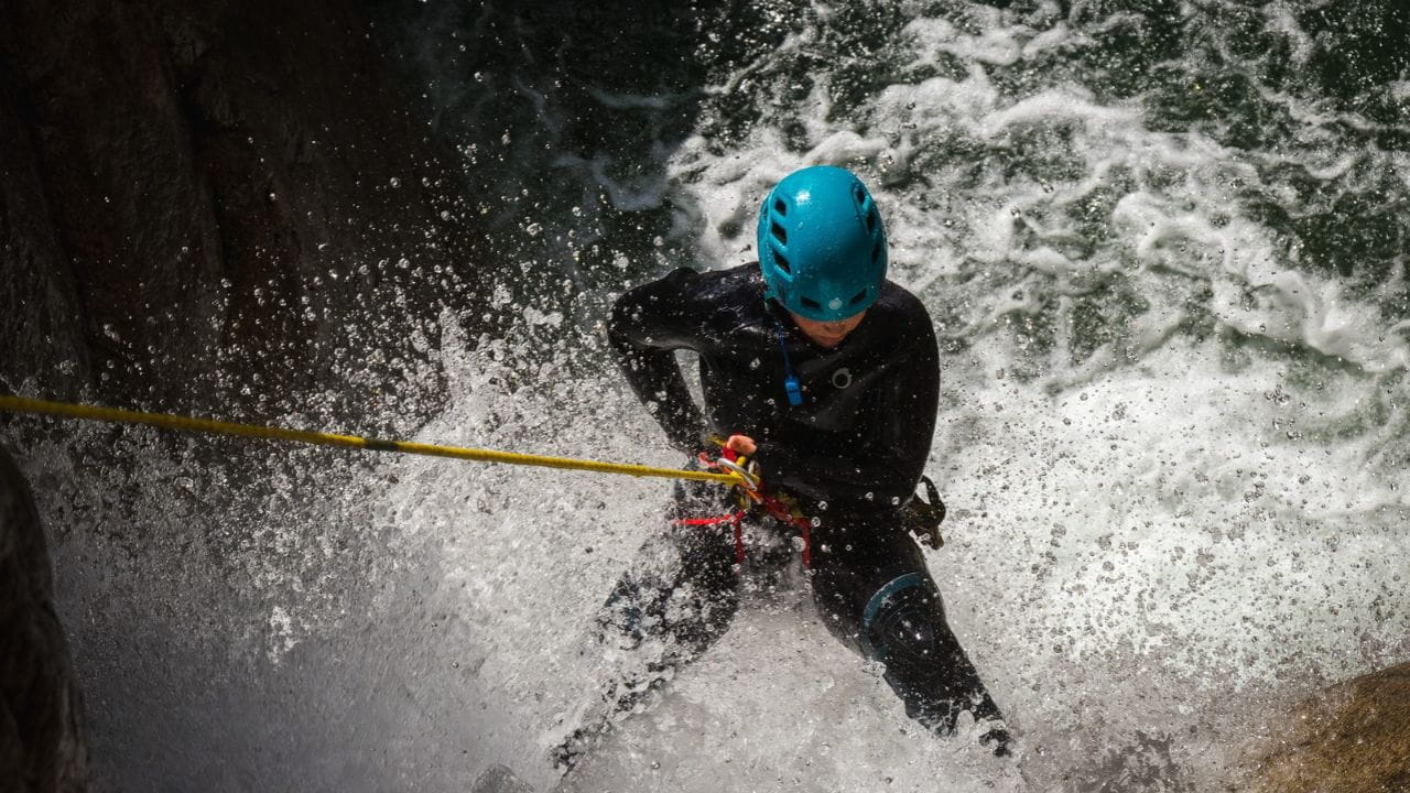 A canyoner abseiling through the spray of a powerful waterfall on a yellow rope