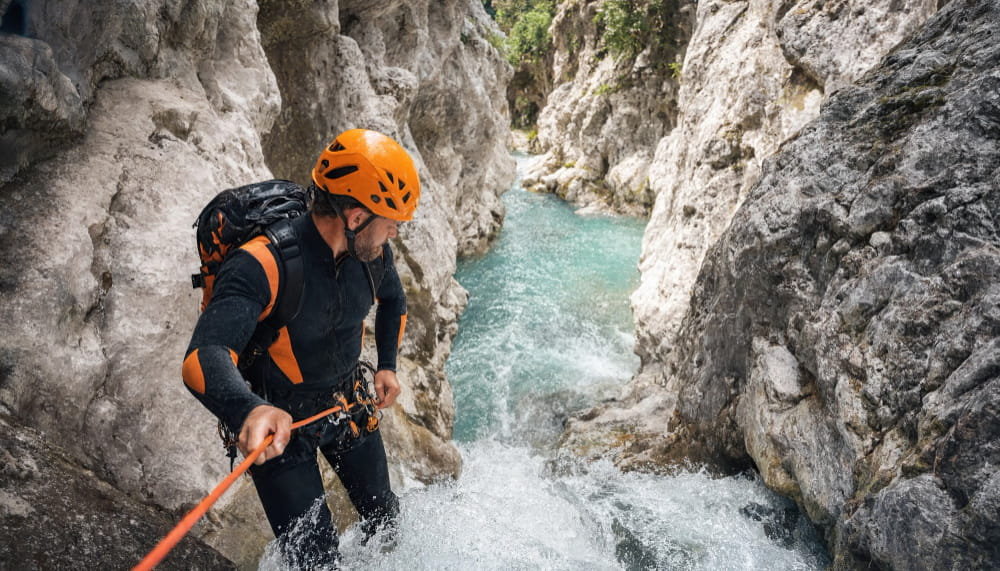 A canyoner abseiling down a waterfall into turquoise water in a European gorge